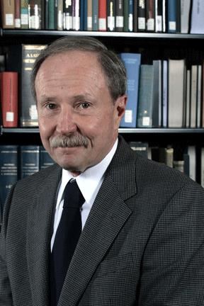 Gerald L Bepko standing in front of a bookshelf.